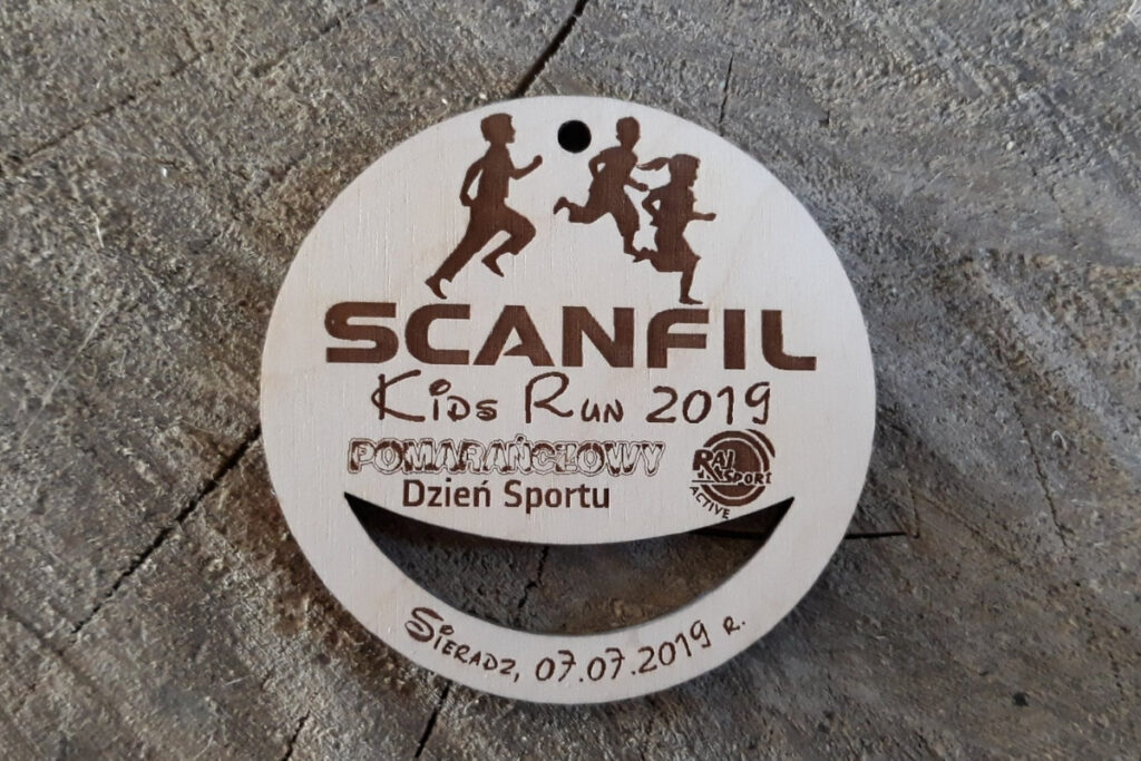 krągły drewniany medal z kolorowym logotypem Scanfil Kids Run, grawerem biegnącego dziecka i napisem Dzień Sportu.