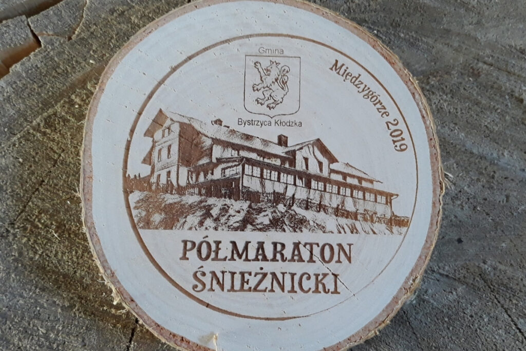 Medal z naturalnego plastra brzozy z grubą korą, grawerem logotypu Półmaratonu Śnieżnickiego i datą edycji.