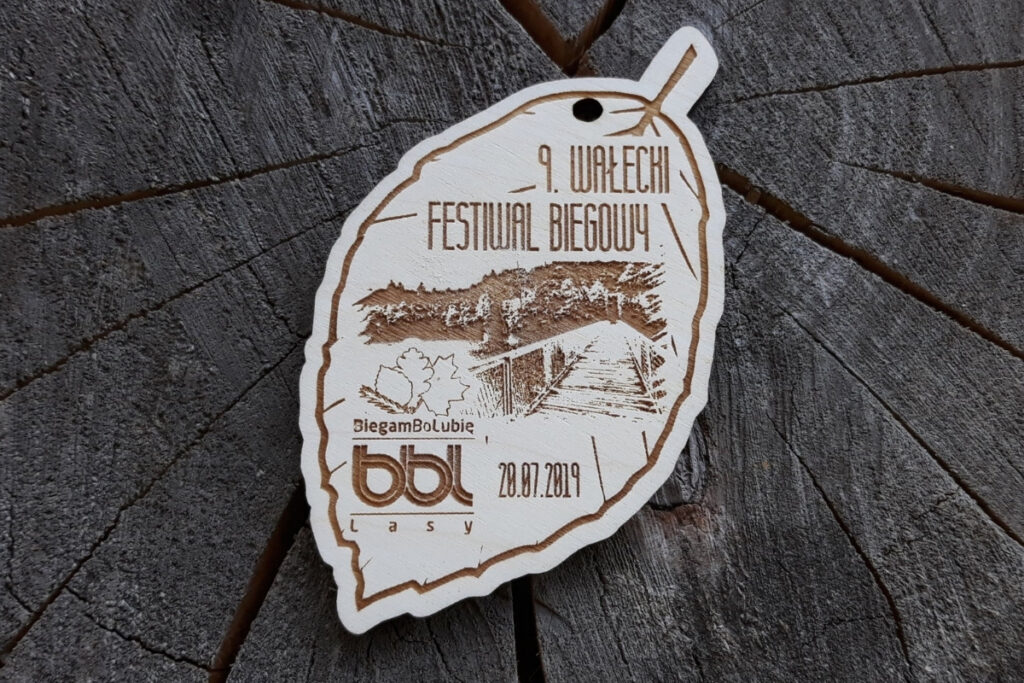 Drewniany medal wycięty w kształcie liścia dębu z grawerem logotypu Wałeckiego Festiwalu Biegowego.