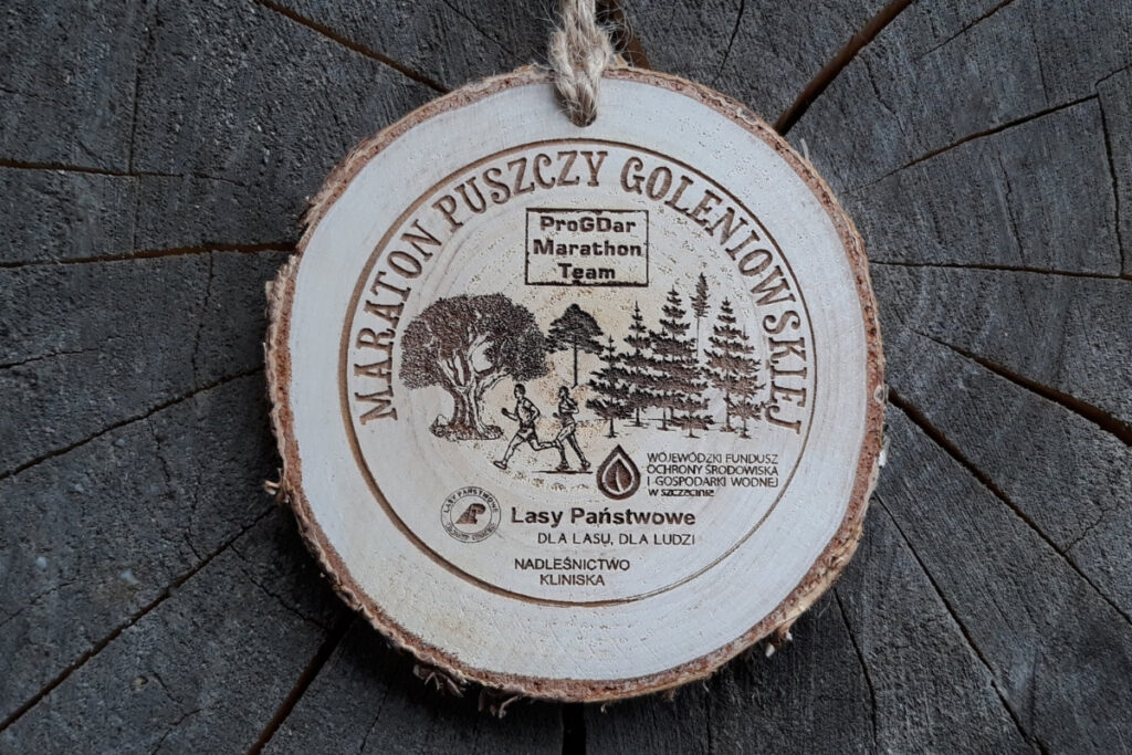 Medal z naturalnego plastra brzozy z korą, z grawerem panoramy lasu, biegacza oraz napisem Maraton Puszczy Goleniowskiej.