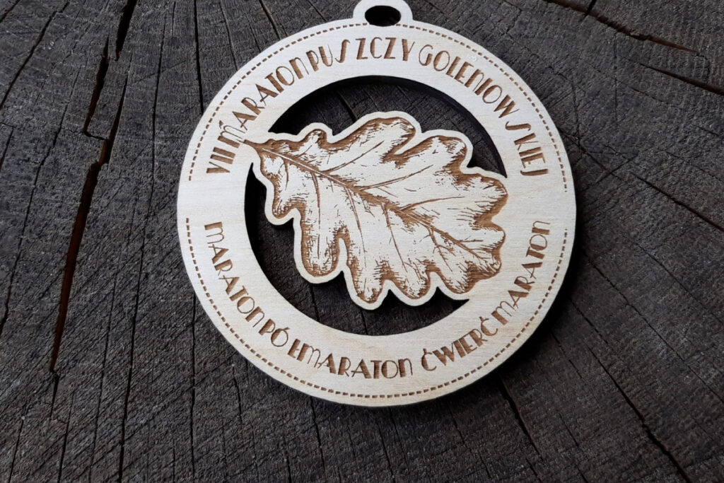 Okrągły drewniany medal z ażurowo wyciętą sylwetką liścia dębu w centralnej części, grawerowaną nazwą Maraton Puszczy Goleniowskiej i datą.