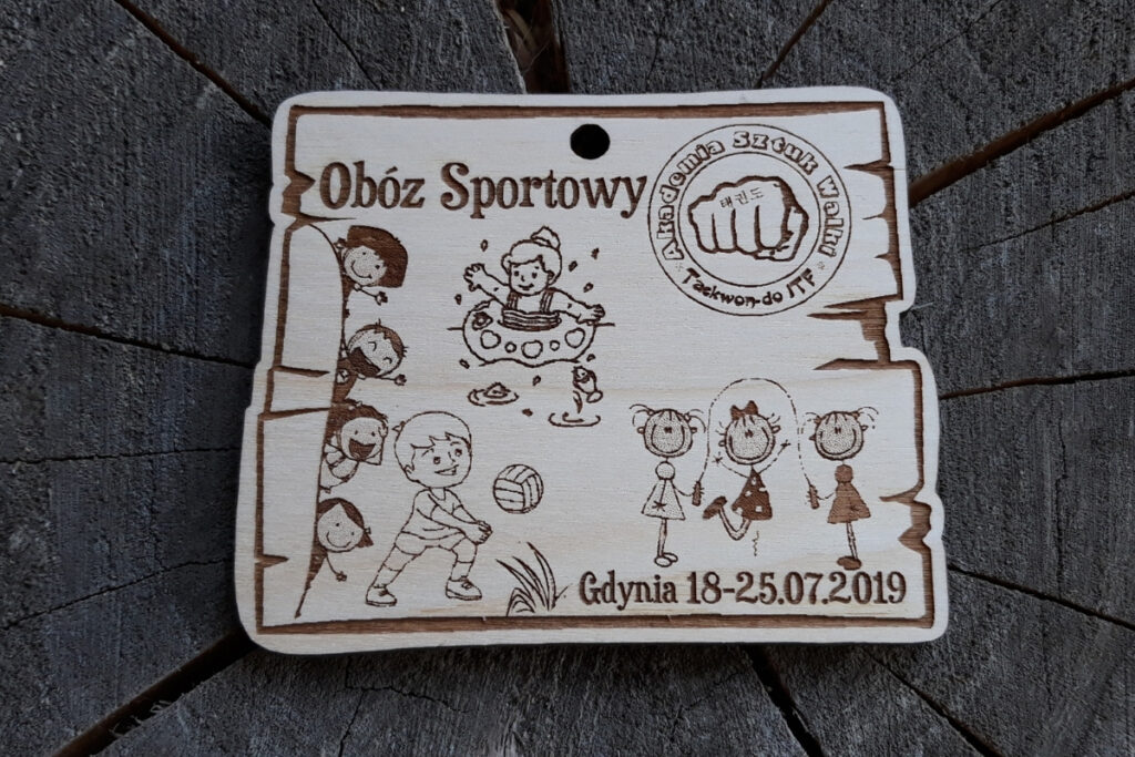 Drewniany medal dla dzieci z grawerem dzieci grających w piłkę, siatkę, badmintona, koszykówkę, logotypem i napisami.