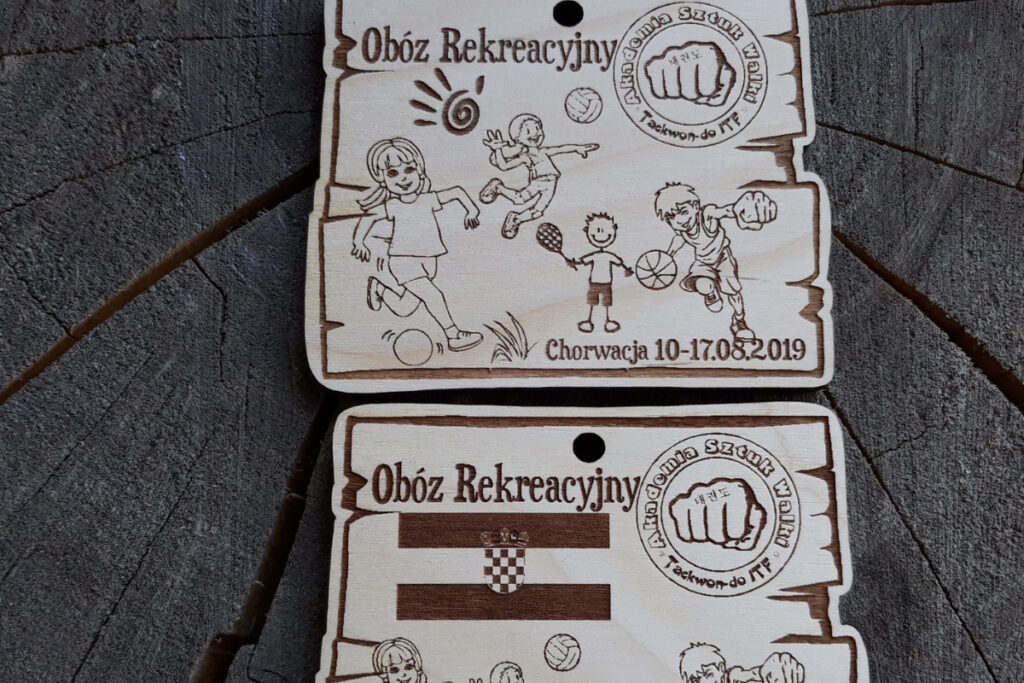 Drewniany medal dla dzieci z grawerem dzieci grających w piłkę, siatkę, badmintona, koszykówkę, logotypem i napisami.