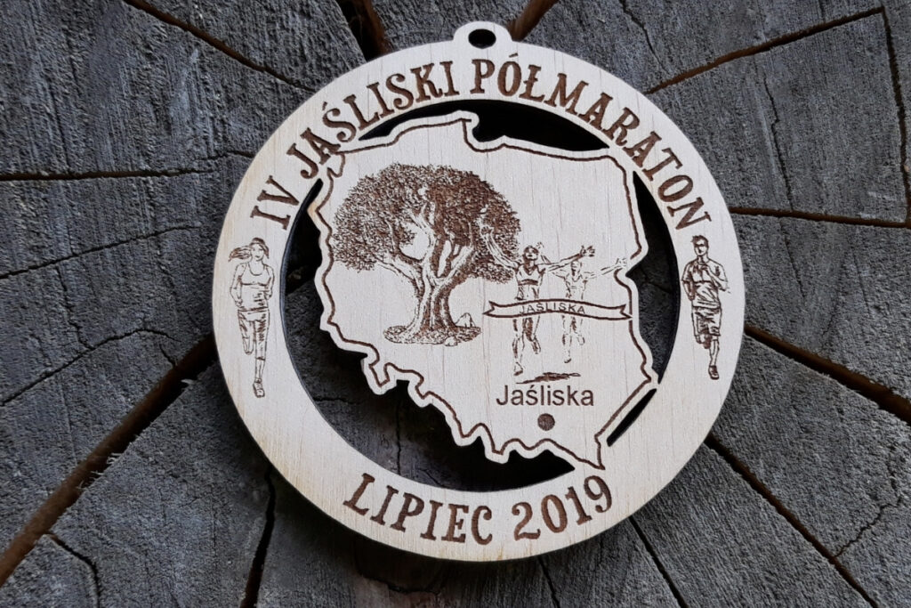 Okrągły drewniany medal z ażurowo wyciętym wewnątrz konturem Polski, grawerem IV Jaśliski Półmaraton oraz datą i lokalizacją biegu.