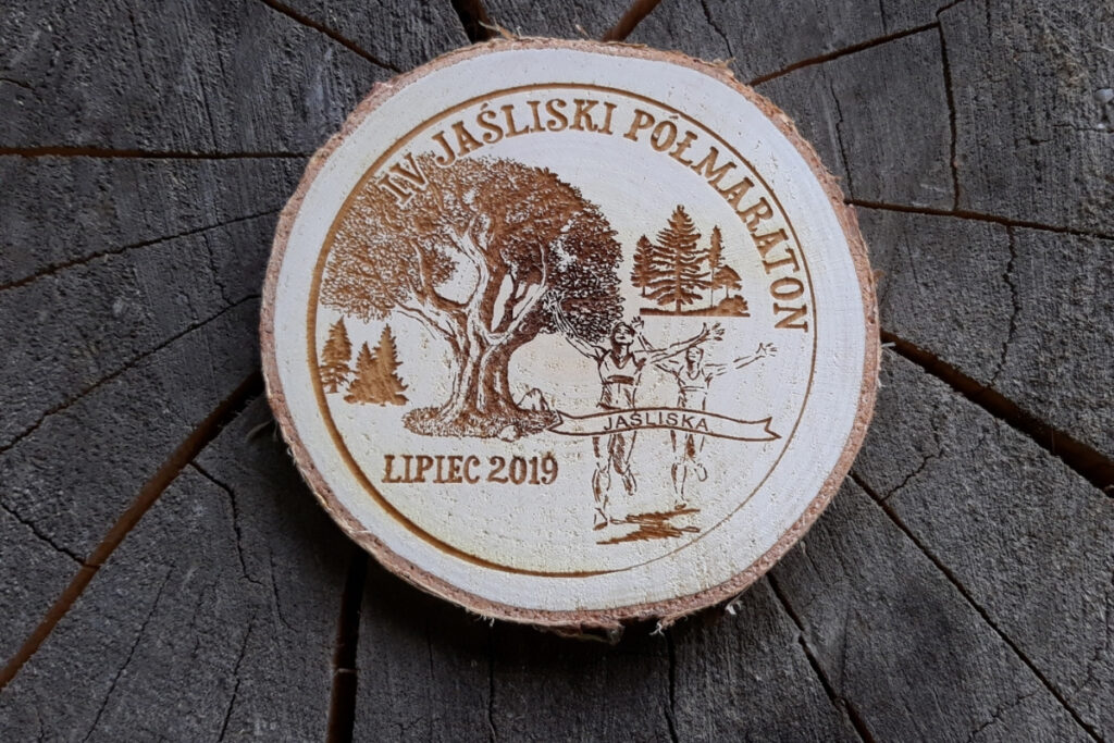 Medal z naturalnego plastra brzozy z korą, grawerem logotypu Jaśliskiego Półmaratonu i sylwetką biegacza na tle drzew.