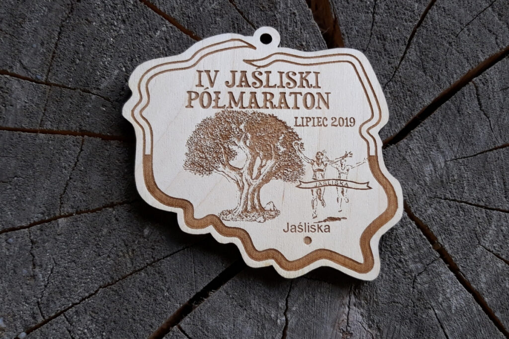 Drewniany medal w nieregularnym kształcie granic Polski, z grawerem IV Jaśliski Półmaraton oraz zaznaczoną gwiazdką lokalizacją Jaślisk.