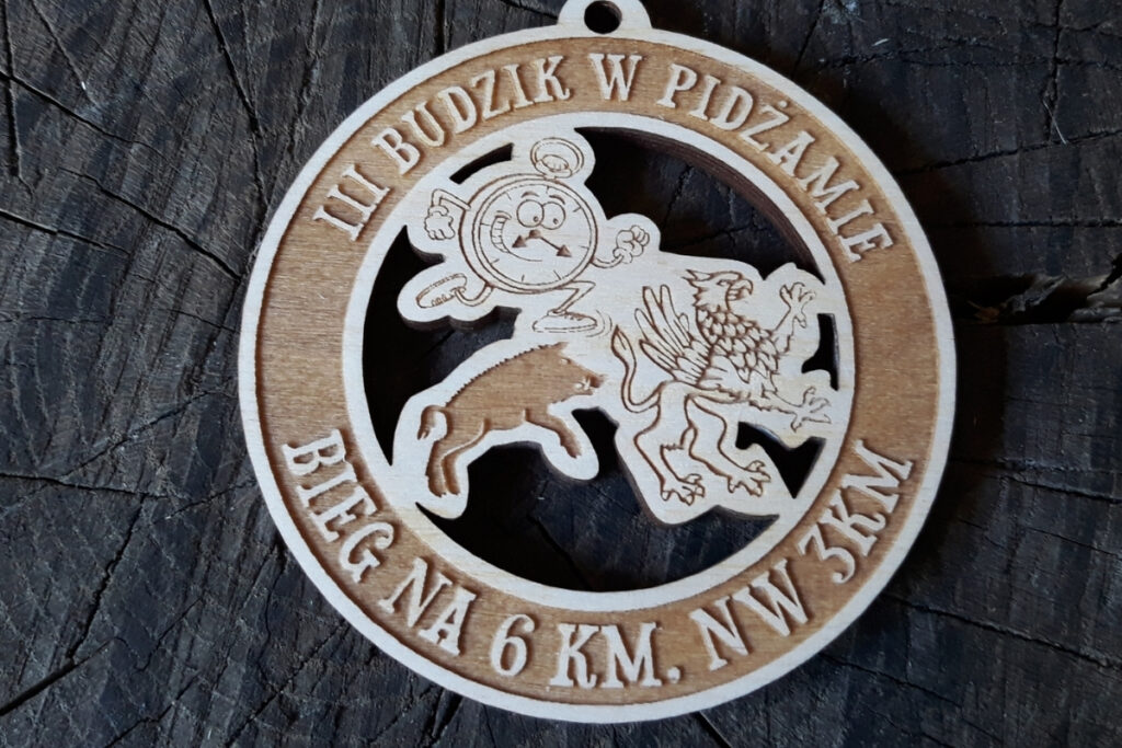 Okrągły drewniany medal ażurowy z wyciętym motywem budzika, napisem III Budzik w Pidżamie oraz logotypem akcji charytatywnej.