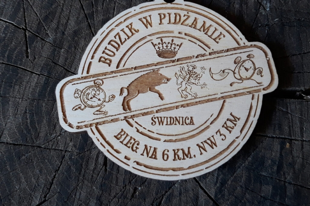 Okrągły drewniany medal z grawerem budzika, napisem Bieg Budzika, medal charytatywny.