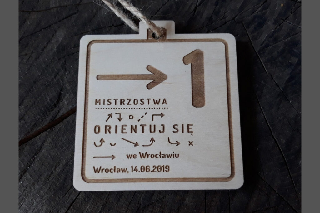 Drewniany medal z grawerem zajętego miejsca, punktów kontrolnych BnO i napisem Mistrzostwa Orientuj Się we Wrocławiu.