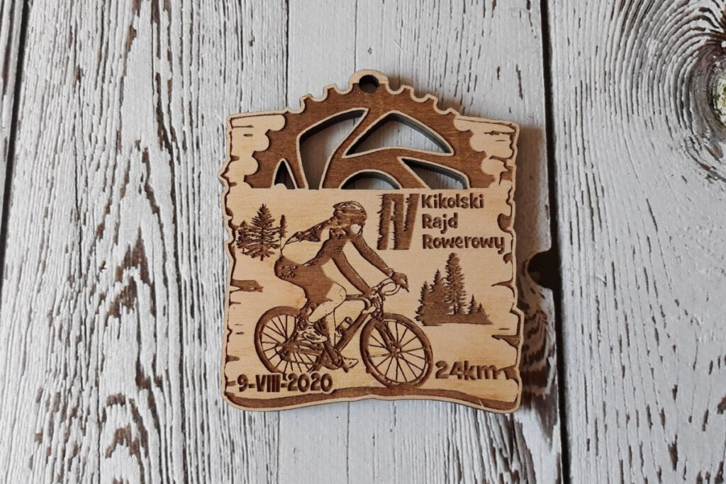 Drewniany medal na rajd rowerowy z ażurowo wyciętym motywem trybu zębatego u góry oraz grawerem rowerzysty w centrum, wykonany z czystej płyty brzozy bez śladów przypaleń.