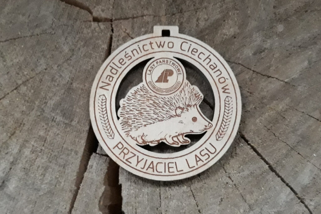 
Okrągły drewniany medal ażurowy „Przyjaciel Lasu” z precyzyjnie wyciętą sylwetką jeża, wykonany z jasnej brzozy bez osmaleń, zawieszony na ekologicznym sznurku jutowym.