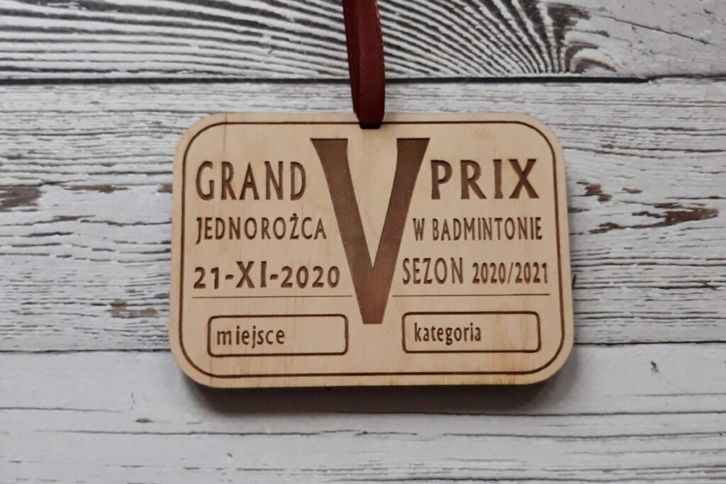 Drewniany medal na V Grand Prix Jednorożca w Badmintonie z grawerem lotki, logotypem wydarzenia oraz specjalnym miejscem na wpisanie zajętego miejsca i kategorii, czyste wykończenie bez osmaleń.