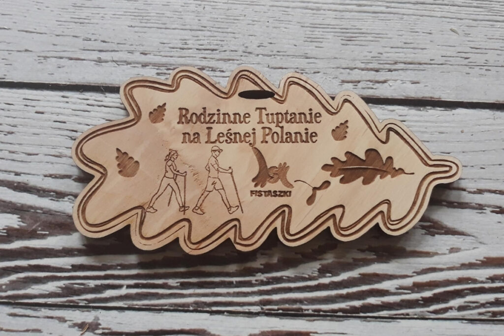 Drewniany medal w kształcie liścia na wydarzenie „Rodzinne Tuptanie”, z grawerem logotypu akcji, wykonany z jasnej, czystej brzozy bez osmaleń, zawieszony na ekologicznym sznurku.