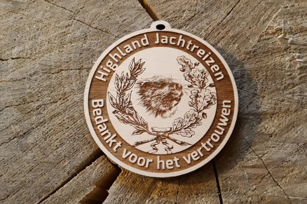 Okrągły drewniany medal myśliwski z grawerem bobra przy żerowisku, ozdobną gałązką dębu oraz napisem okolicznościowym, wykonany z jasnej brzozy bez śladów dymu.