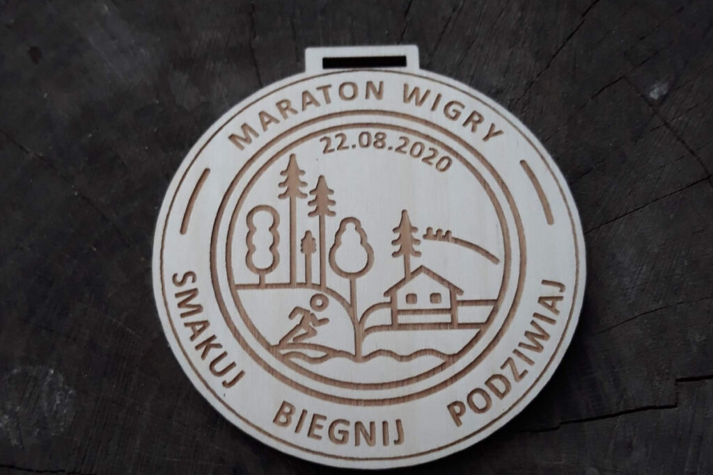 Okrągły drewniany medal na Maraton Wigry z hasłem „Smakuj, Biegnij, Podziwiaj”, wykonany z czystej brzozy bez śladów dymu.