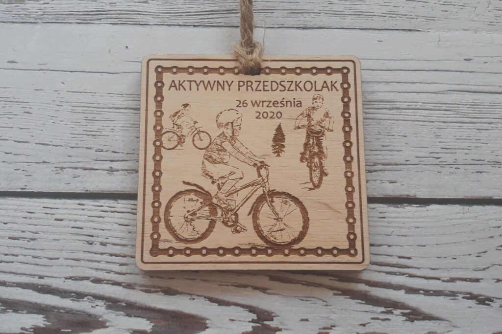 Prostokątny drewniany medal dla dzieci na zawody „Aktywny Przedszkolak”, z grawerem dziecka na rowerze, wykonany z czystej płyty brzozy bez osmaleń.