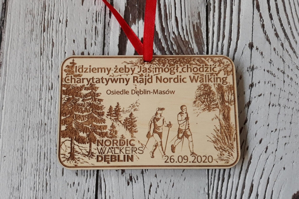 Prostokątny drewniany medal na Charytatywny Marsz Nordic Walking z grawerem pary maszerującej z kijkami,  oraz inspirującym cytatem o pomaganiu, wykonany z jasnej brzozy bez śladów dymu.