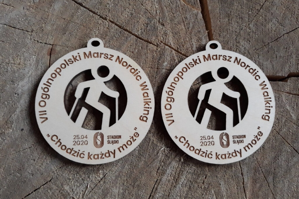Okrągły drewniany medal na Ogólnopolski Rajd Nordic Walking „Chodzić każdy może”, z ażurowo wyciętą sylwetką osoby maszerującej z kijkami oraz grawerem logotypu wydarzenia, wykonany z czystej brzozy bez śladów dymu.