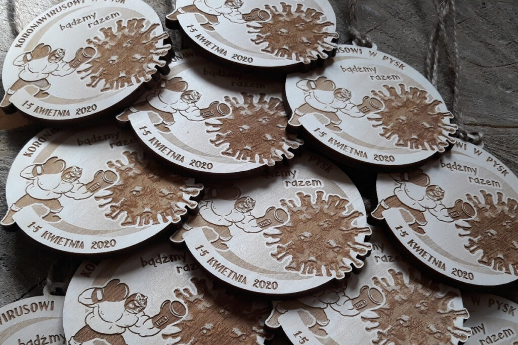 Okrągły drewniany medal z akcji „Koronawirusowi w pysk”, z grawerem zaciśniętej pięści uderzającej w symbol wirusa, oraz datą, wykonany z czystej brzozy bez śladów dymu.