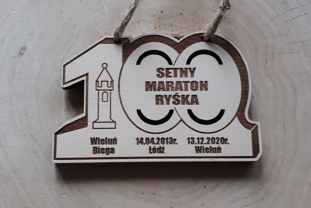 Drewniany medal jubileuszowy na „Setny Maraton Ryśka”. Medal w kształcie cyfry 100, wykonany z czystej brzozy bez śladów przypaleń.