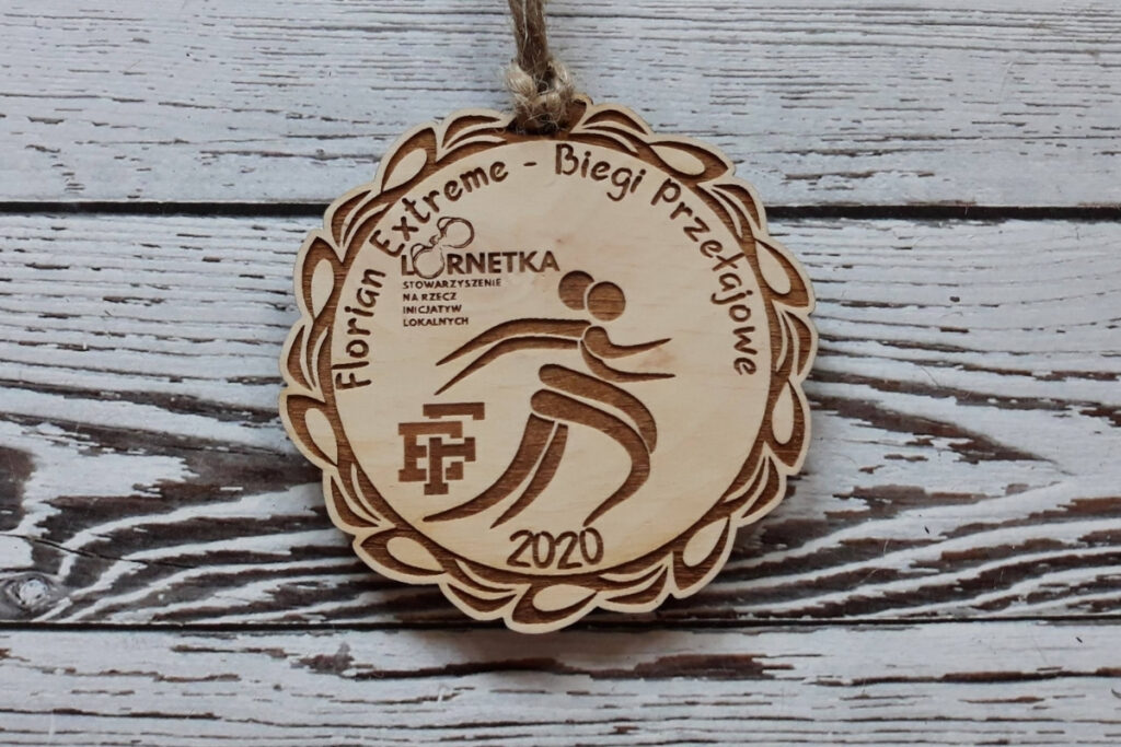 Okrągły drewniany medal na biegi przełajowe Florian Extreme, z grawerem płomieni, logotypem wydarzenia oraz dynamiczną czcionką, wykonany z jasnej brzozy bez śladów osmaleń.