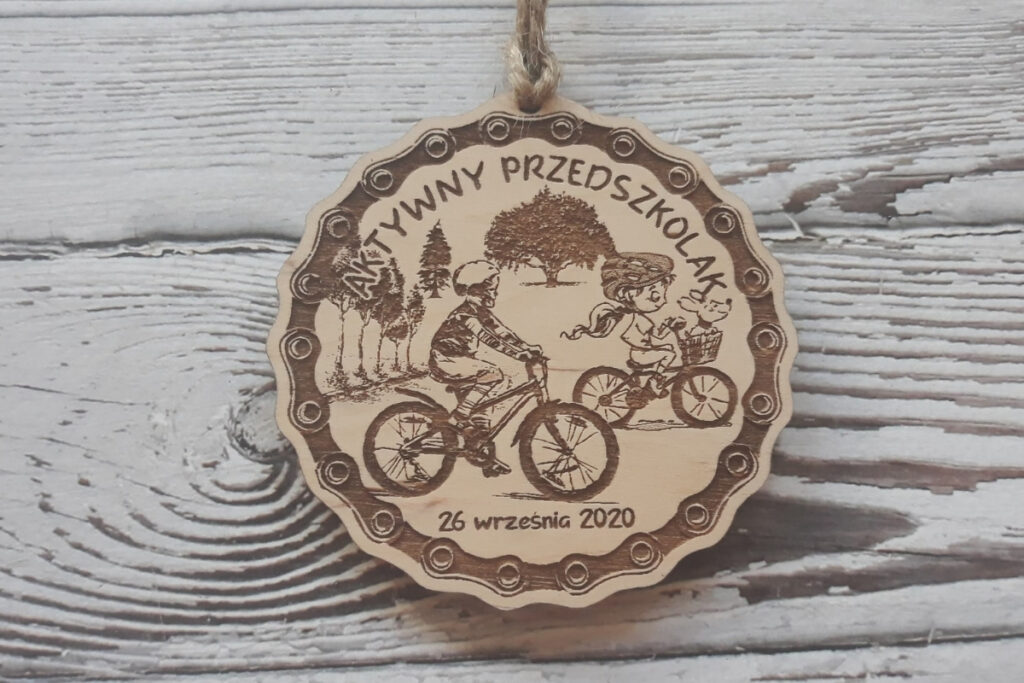 Okrągły drewniany medal dla dzieci z grawerem dziecka  w kasku na rowerze, napisem Aktywny Przedszkolak oraz datą.