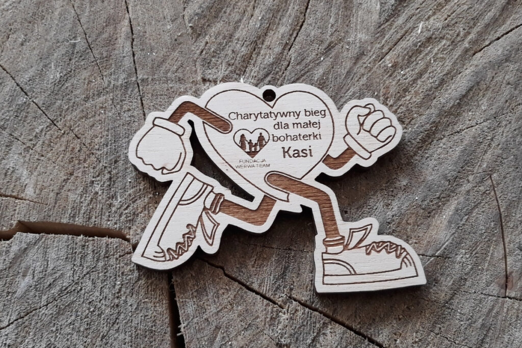 Drewniany medal w kształcie serca z rękami i nogami, które biegnie. Medal na bieg charytatywny.
