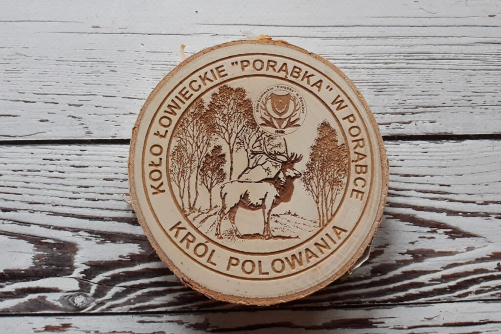 Drewniany medal na plastrze brzozy z naturalną korą dla Koła Łowieckiego, z grawerem dumnego jelenia byka, napisem „Król Polowania” oraz logotypem koła, czysta powierzchnia bez przypaleń.