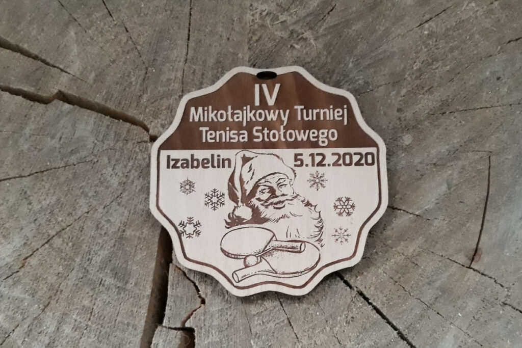 Okrągły drewniany medal na Mikołajkowy Turniej Tenisa Stołowego, z grawerem rakietki, piłeczki oraz twarzy i czapki św. Mikołaja, wykonany z płyty - jasnej brzozy bez śladów dymu.