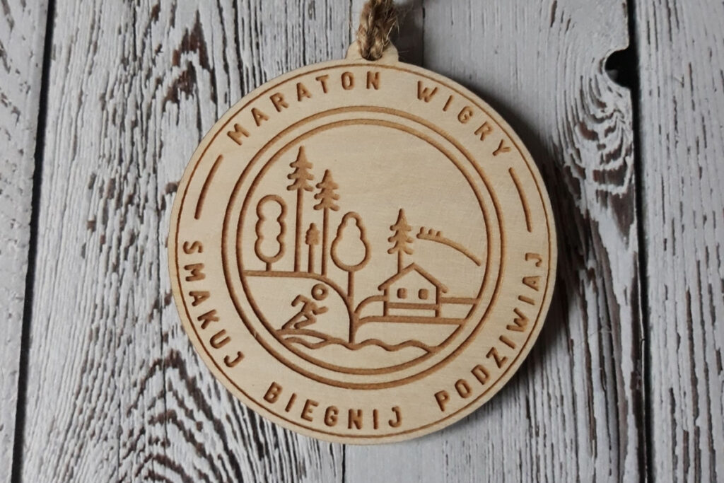 Okrągły drewniany medal na Maraton Wigry z hasłem „Smakuj, Biegnij, Podziwiaj”, wykonany z czystej brzozy bez śladów dymu.