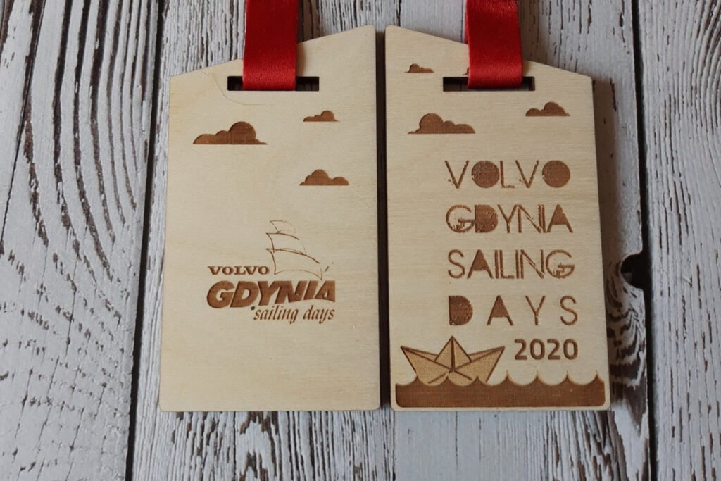 Drewniany medal na Volvo Gdynia Sailing Days 2020, z grawerem logotypu wydarzenia, sylwetką żaglówki na falach oraz logotypami partnerów, wykonany z płyty jasnej brzozy bez śladów dymu.
