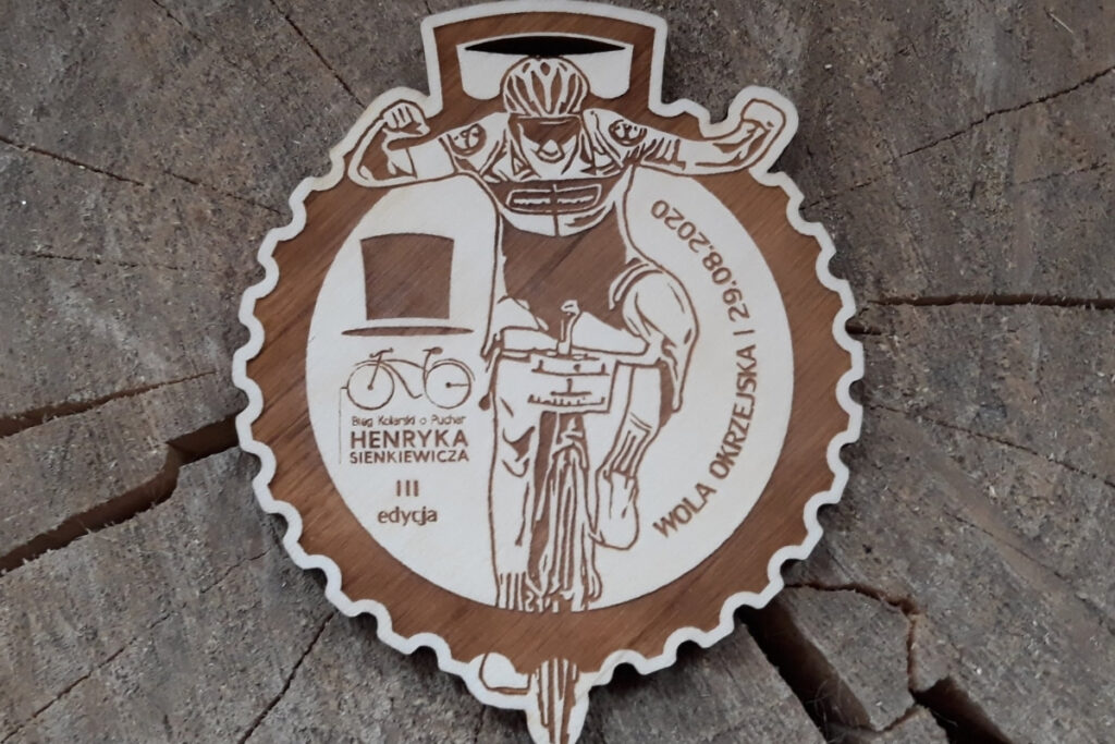 Okrągły drewniany medal na wyścig kolarski, z grawerem kolarza w dynamicznej jeździe, zębatki rowerowej oraz miejsca na nazwę zawodów, wykonany z czystej brzozy bez śladów przypaleń.