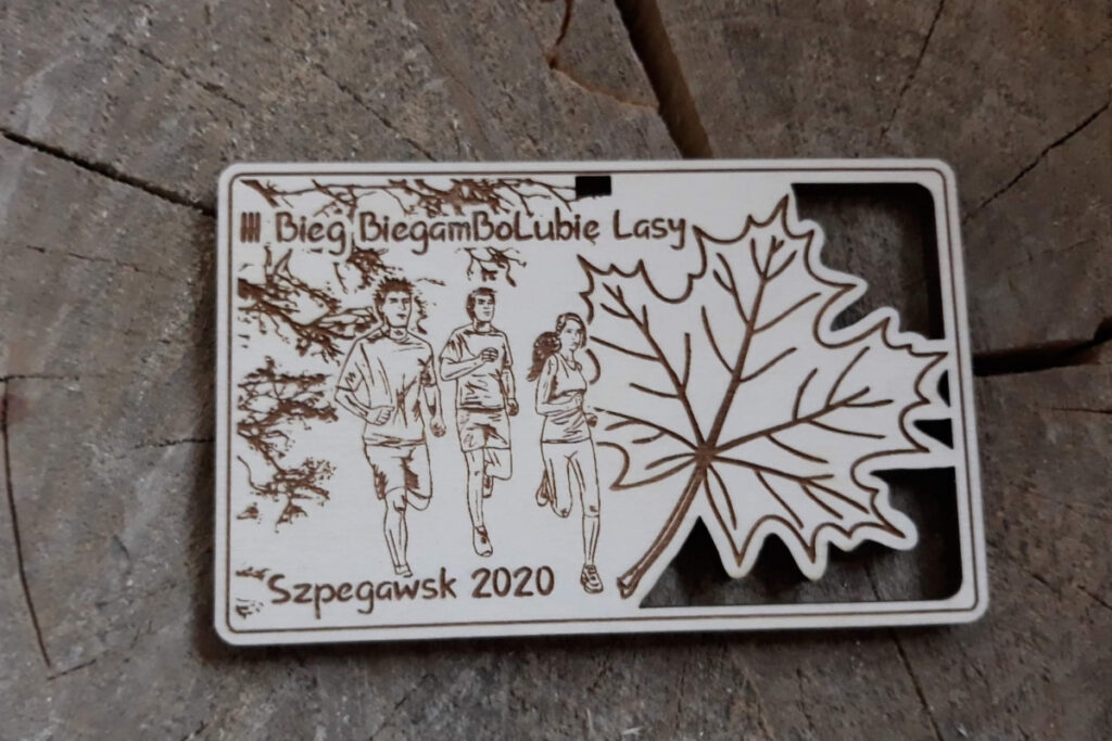 Prostokątny drewniany medal na bieg leśny z precyzyjnie wyciętym ażurowym liściem klonu, grawerem leśnego krajobrazu oraz miejscem na logo zawodów, wykonany z czystej brzozy bez osmaleń.
