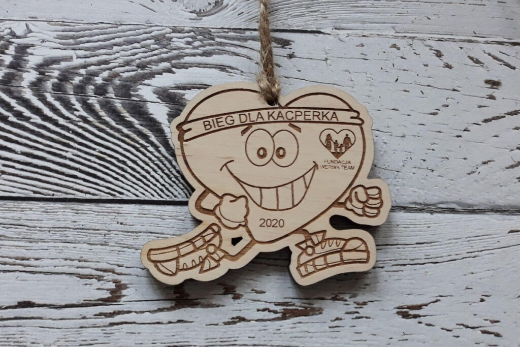 Drewniany medal na bieg charytatywny z grawerem „Biegnącego Serca” w butach sportowych, napisem „Bieg dla Kacperka” oraz miejscem na logo fundacji, wykonany z czystej brzozy bez śladów dymu.sklejki brzozowej.