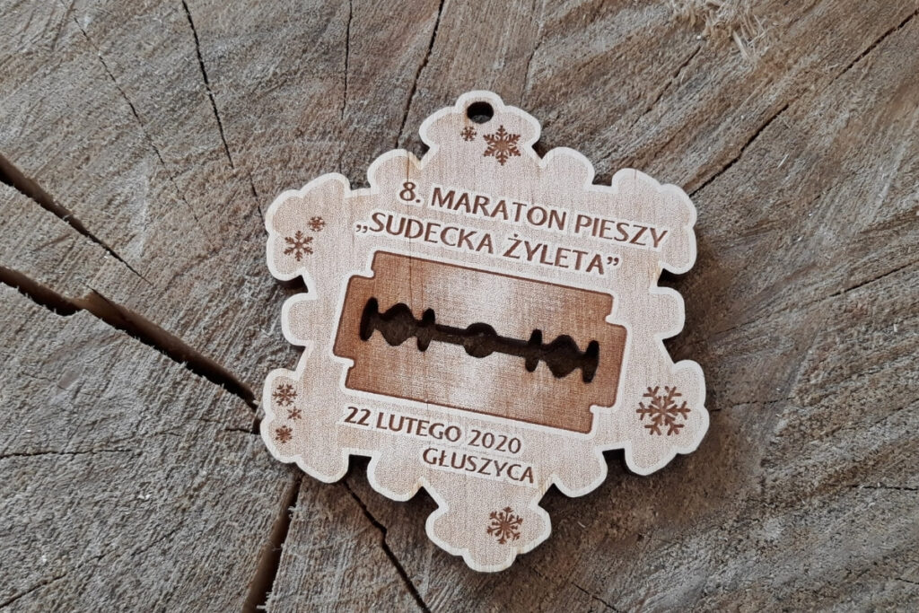 Drewniany medal w kształcie płatka śniegu z żyletką w środku.
