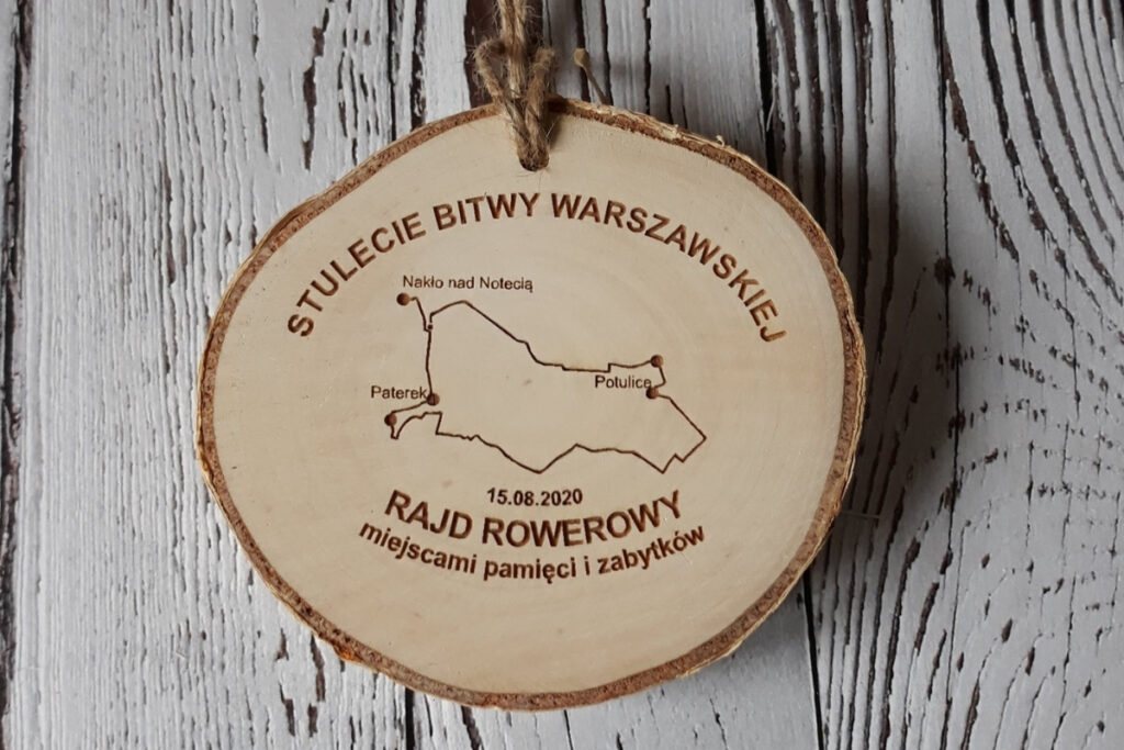 Drewniany medal na naturalnym plastrze brzozy z korą, upamiętniający Rajd na 100-lecie Bitwy Warszawskiej, z grawerem daty, prostej mapki, oraz napisem okolicznościowym, czysta powierzchnia bez osmaleń.