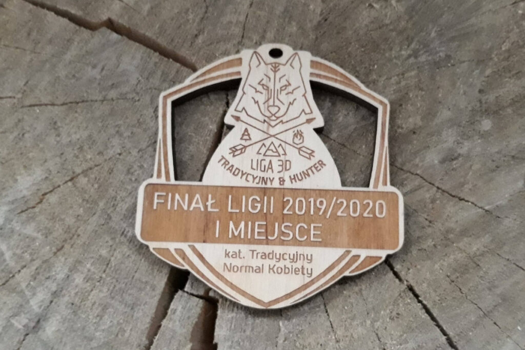 Drewniany medal łuczniczy z ażurowym wycięciem logotypu Ligi, precyzyjnym grawerem oraz napisem okolicznościowym, wykonany z jasnej brzozy bez śladów dymu.