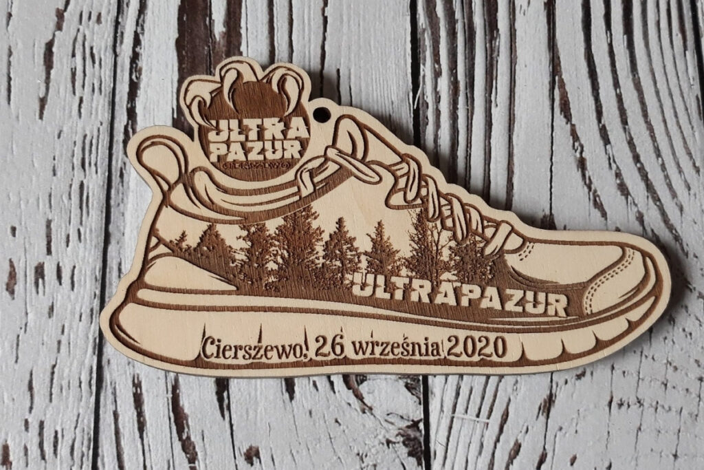 Drewniany medal w kształcie buta sportowego do biegów leśnych, z grawerem bieżnika, sznurowadeł oraz motywem drzew iglastych, wykonany z czystej brzozy bez osmaleń.