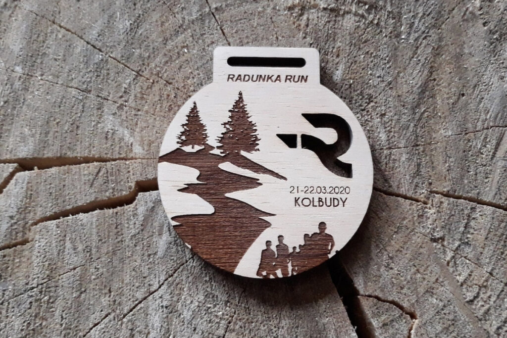 Okrągły drewniany medal na bieg „Radunka Run”, z grawerem sylwetek biegaczy, nazwą zawodów oraz ażurowym logotypem