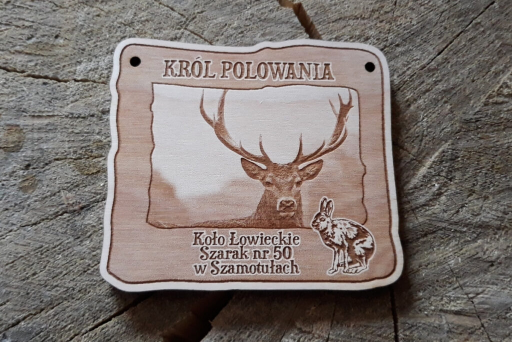 Prostokątny drewniany medal dla Króla Polowania z precyzyjnym grawerem potężnego jelenia byka oraz zająca szaraka, napisem „Król Polowania” i miejscem na nazwę Koła Łowieckiego, wykonany z czystej brzozy bez osmaleń.