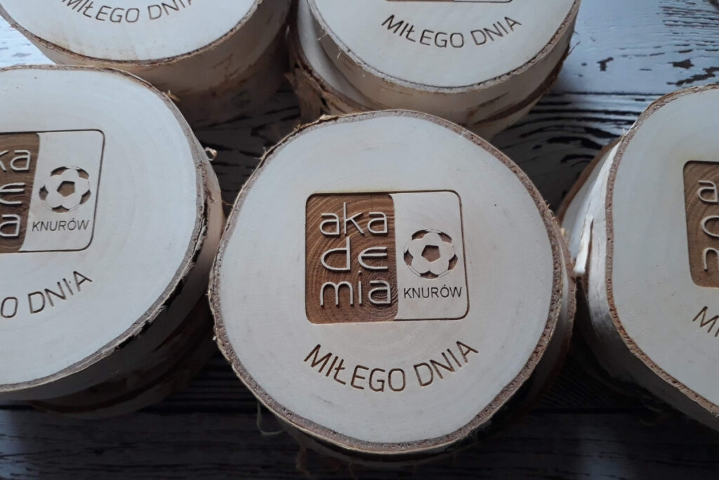 Drewniany medal na naturalnym plastrze brzozy z korą dla młodych piłkarzy, z grawerem loga Akademii Piłkarskiej oraz półokrągłym napisem na dole miłego dnia.