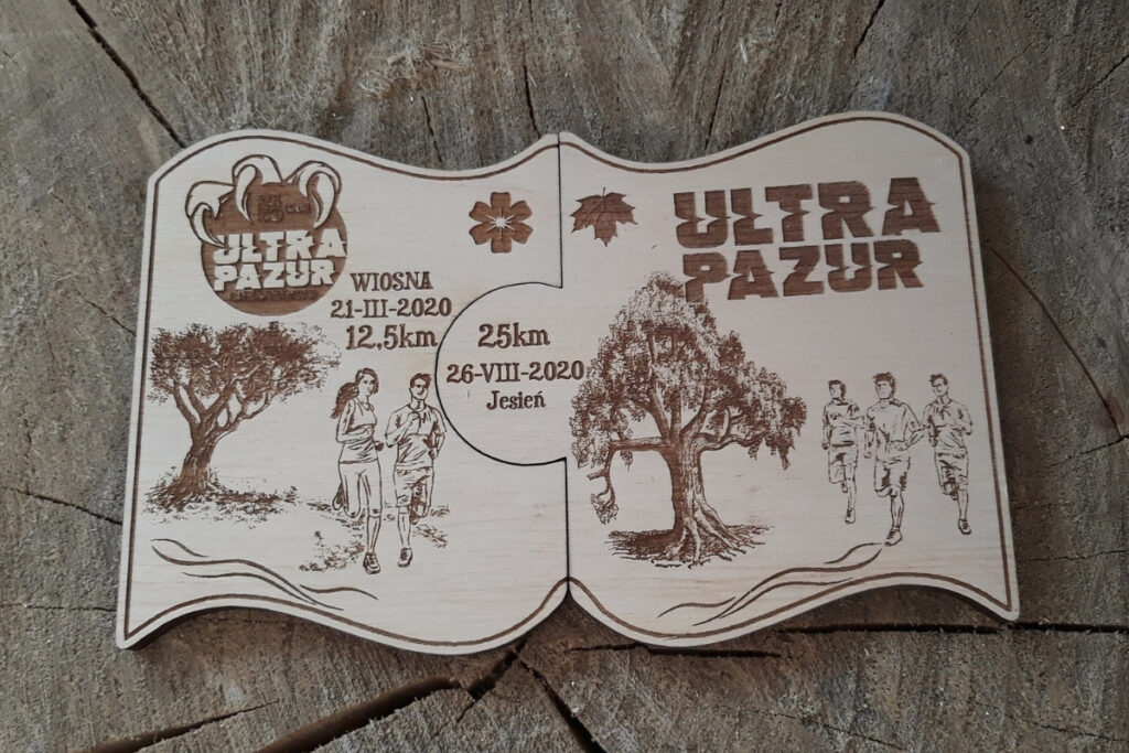 Zestaw dwóch drewnianych medali modułowych „Ultra Pazur”, które dzięki precyzyjnemu wycięciu typu puzzle łączą się w jedną spójną tabliczkę, z grawerem drapieżnych śladów pazurów i dynamicznym logotypem biegu, wykonany z czystej brzozy bez osmaleń. Na grafice drzewa, biegacze, napis.
