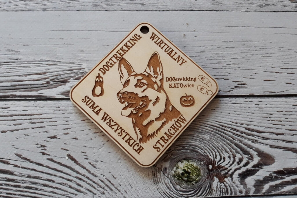 Trapezowy drewniany medal na zawody dogtrekkingowe, z grawerem głowy psa oraz nazwą wydarzenia, wykonany z czystej brzozy bez śladów dymu i osmaleń.