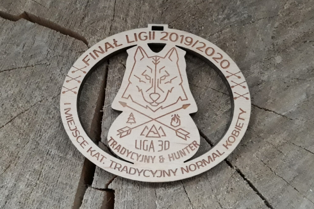 Drewniany medal łuczniczy z ażurowym wycięciem logotypu Ligi, precyzyjnym grawerem oraz napisem okolicznościowym, wykonany z jasnej brzozy bez śladów dymu.