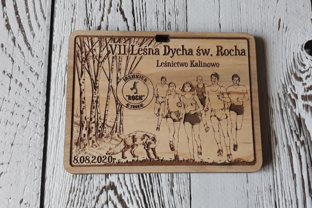 Prostokątny drewniany medal na bieg „VII Dycha św. Rocha”, z grawerem leśnych motywów, liściastych drzew i gałązek oraz logotypem wydarzenia, wykonany z czystej brzozy o naturalnie jasnej powierzchni bez osmaleń.