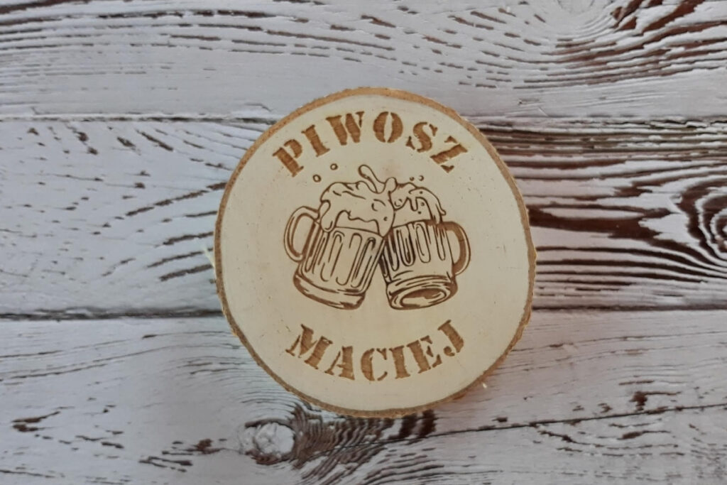 Okrągła drewniana podstawka pod kufel z grawerem „Piwosz Maciej”, grafiką pienistego kufla piwa, wykonana z jasnej sklejki brzozowej bez śladów dymu i osmaleń.