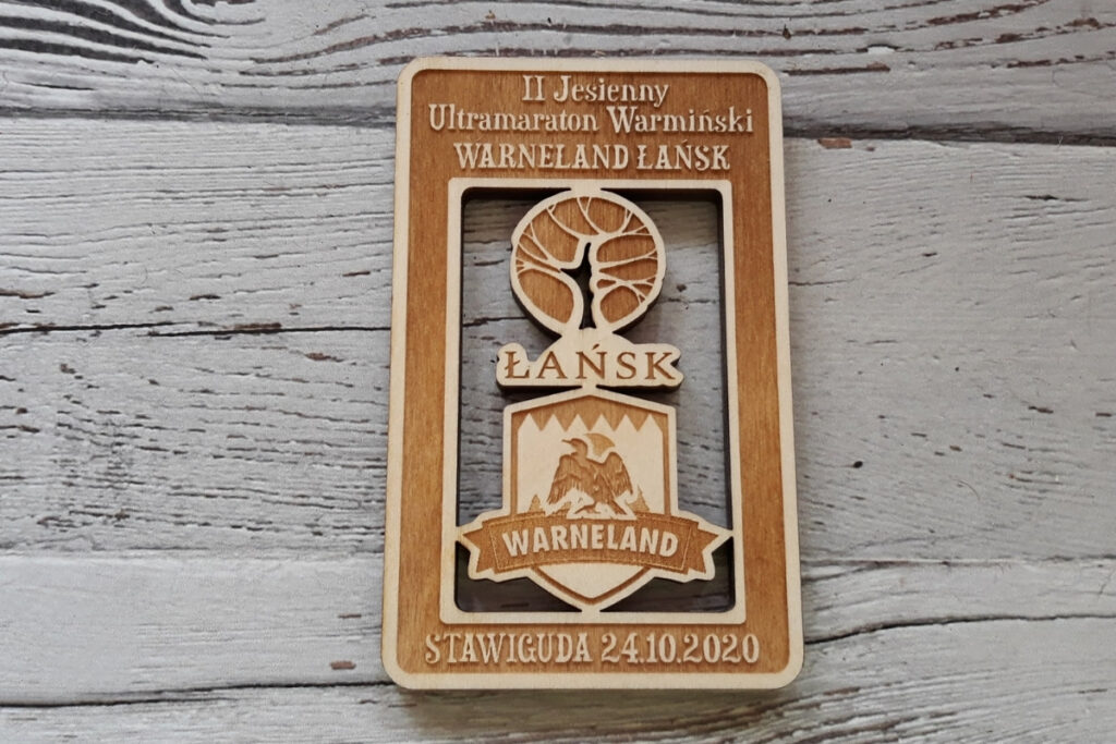 Prostokątny medal z ażurowo wyciętym logiem Łańska i Warneland. U dołu napis Stawiguda.