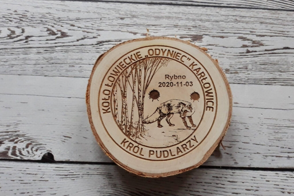 Drewniany medal na naturalnym plastrze brzozy z korą dla „Króla Pudlarzy”, z grawerem siedzącego lisa, wieńca z liści dębu oraz napisu okolicznościowego, wykonany bez śladów dymu i osmaleń.