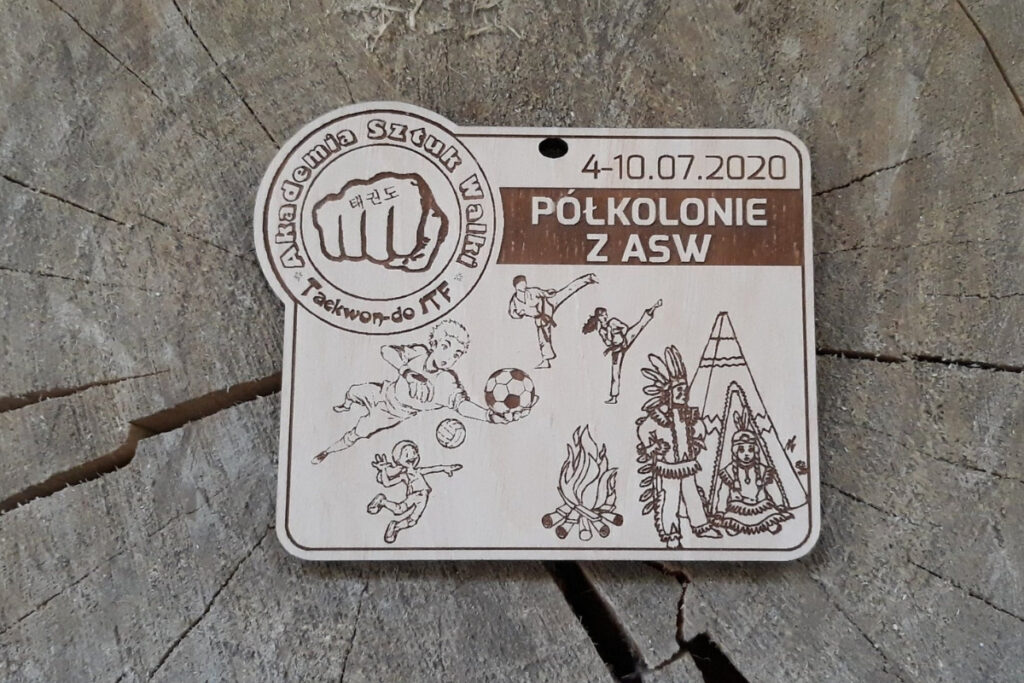 Prostokątny drewniany medal na „Półkolonie z ASW”, z grawerem logotypu Akademii Sztuk Walki, napisem okolicznościowym, wykonany z jasnej brzozy bez śladów dymu i osmaleń. Na medalu dzieci grają w piłkę, ćwiczą taekwon-do, jest ognisko oraz namiot indiański.