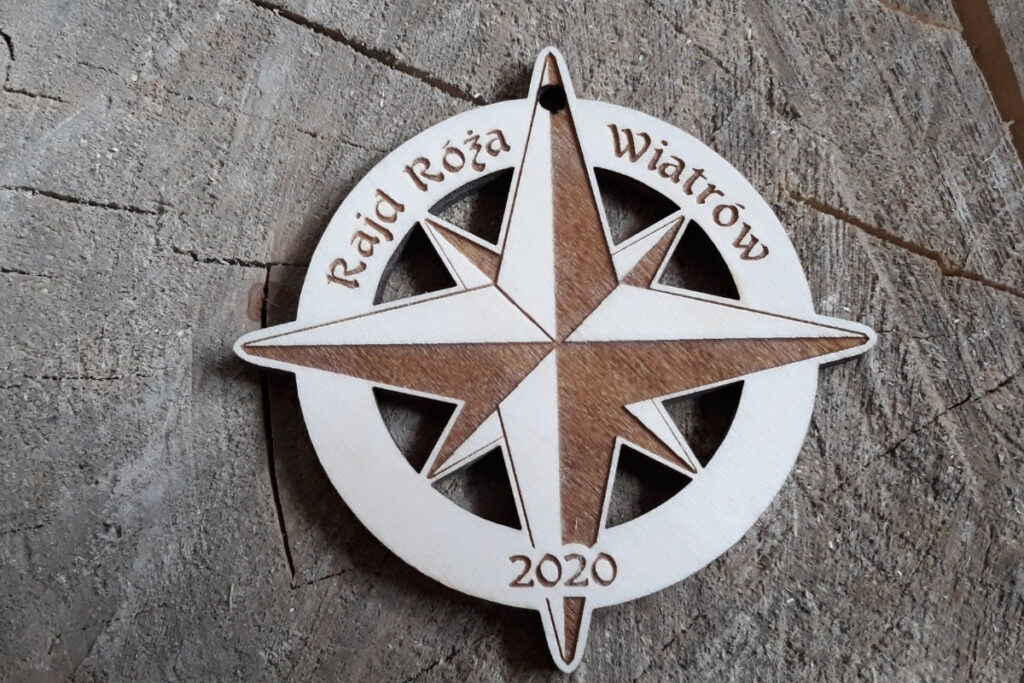 Ażurowy drewniany medal na „Rajd Róża Wiatrów” z precyzyjnie wyciętym wewnątrz motywem róży wiatrów oraz grawerem nazwy rajdu, wykonany z czystej brzozy bez śladów dymu i osmaleń.